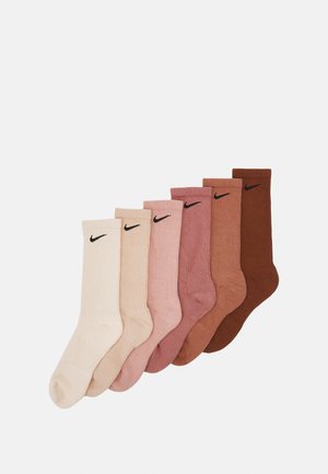 Sett med 7 ribbestrikkede sokker i nyanser av beige, rosa og brun. Hver sokk har en svart Nike-logo øverst. Mykt bomullsmateriale.