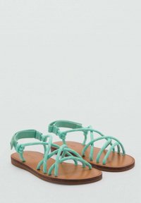 Myntgröna sandaler med remmar och flat brun sula, med flera vävda remmar och ett justerbart bakrem. Slät textur.