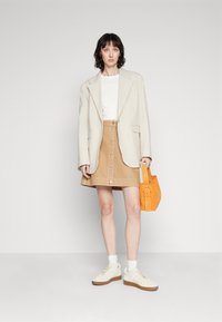 Blazer di lino beige, camicia bianca attillata, gonna in corda color sabbia con bottoni, borsa in suede arancione e sneaker color crema con suole testurizzate.