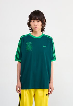 Zöld, rövid ujjú Adidas póló kontrasztos zöld gallérral és ujjvégekkel, elöl az Adidas logóval és grafikai nyomtatott mintákkal.