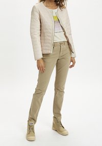 Jasnoróżowa pikowana kurtka z okrągłym kołnierzem, beżowe dopasowane spodnie oraz beżowe buty na sznurowadła. Na bluzce znajduje się nadruk graficzny.