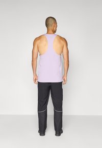 Lichtpaarse tanktop met een racerback ontwerp, gecombineerd met zwarte broek met meshaccenten en een rechte snit.