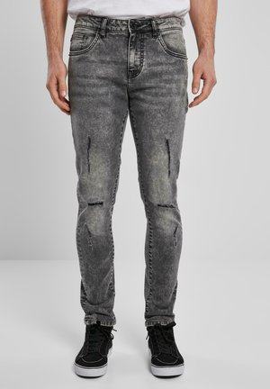 Fadet sorte skinny jeans med slidte detaljer, fem-lomme design og diskret hvid syning, parret med sorte høj-top sneakers.