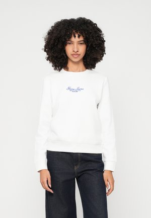 Biely sveter s okrúhlym výstrihom, s modrým vyšívaným textom "Guess Jeans" na hrudníku. Dlhé rukávy a rebrované manžety, v kombinácii s tmavými džínsami.