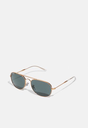 Gafas de sol de metal con marco dorado, lentes tintadas en verde y puntas de patilla transparentes. Forma angular con marca en una lente.