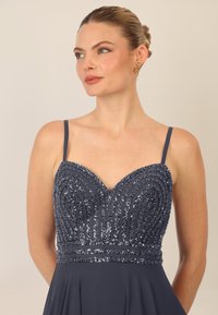 Navyblaues Paillettenkleid mit herzförmigem Ausschnitt, dünnen Trägern und einem fließenden Rock mit aufwendigen Perlendetails entlang des Oberteils.