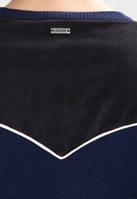 Felpa navy e nera con parte superiore in camoscio, scollatura a costine e piping bianco a contrasto lungo la cucitura. Etichetta del logo sul retro.