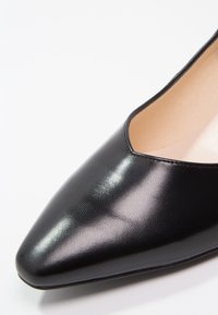 Czarny skórzany but ze spiczastym noskiem, niskim wycięciem, gładką fakturą i błyszczącym wykończeniem; widoczne minimalne przeszycia.