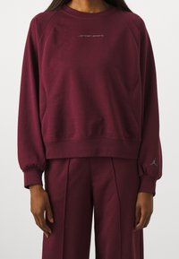 Sudadera burdeos de tejido de mezcla de algodón, con cuello redondo, puños acanalados y logotipo bordado "Jordan Sport" centrado en el pecho.