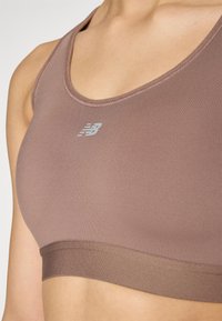 Soutien-gorge de sport marron en tissu lisse, avec une large bande en bas, un décolleté arrondi et un petit logo argenté à l'avant.