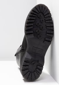 Botte en cuir noir avec une semelle en caoutchouc texturée présentant des crampons profonds et une fermeture éclair latérale, conçue pour l'adhérence et la durabilité.