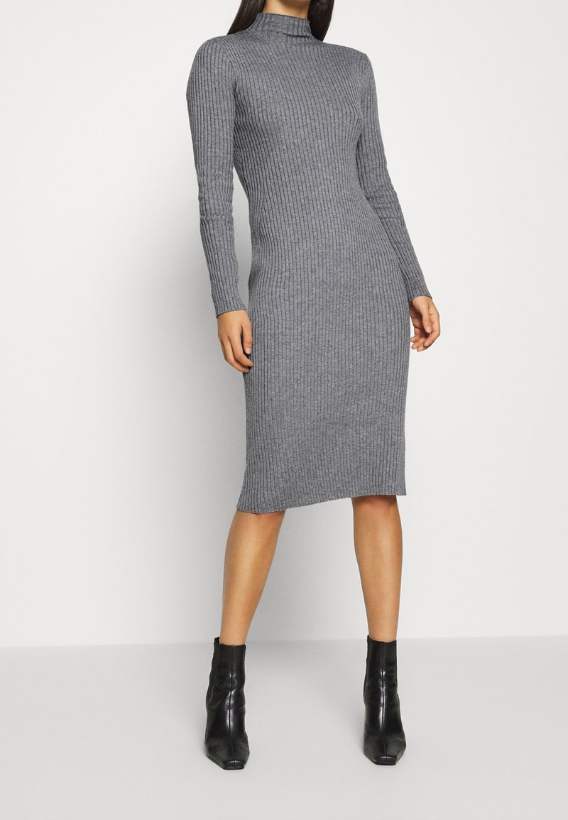 Robe grise à manches longues côtelées avec un col montant, silhouette ajustée et longueur mi-mollet. Associée à des bottines noires.
