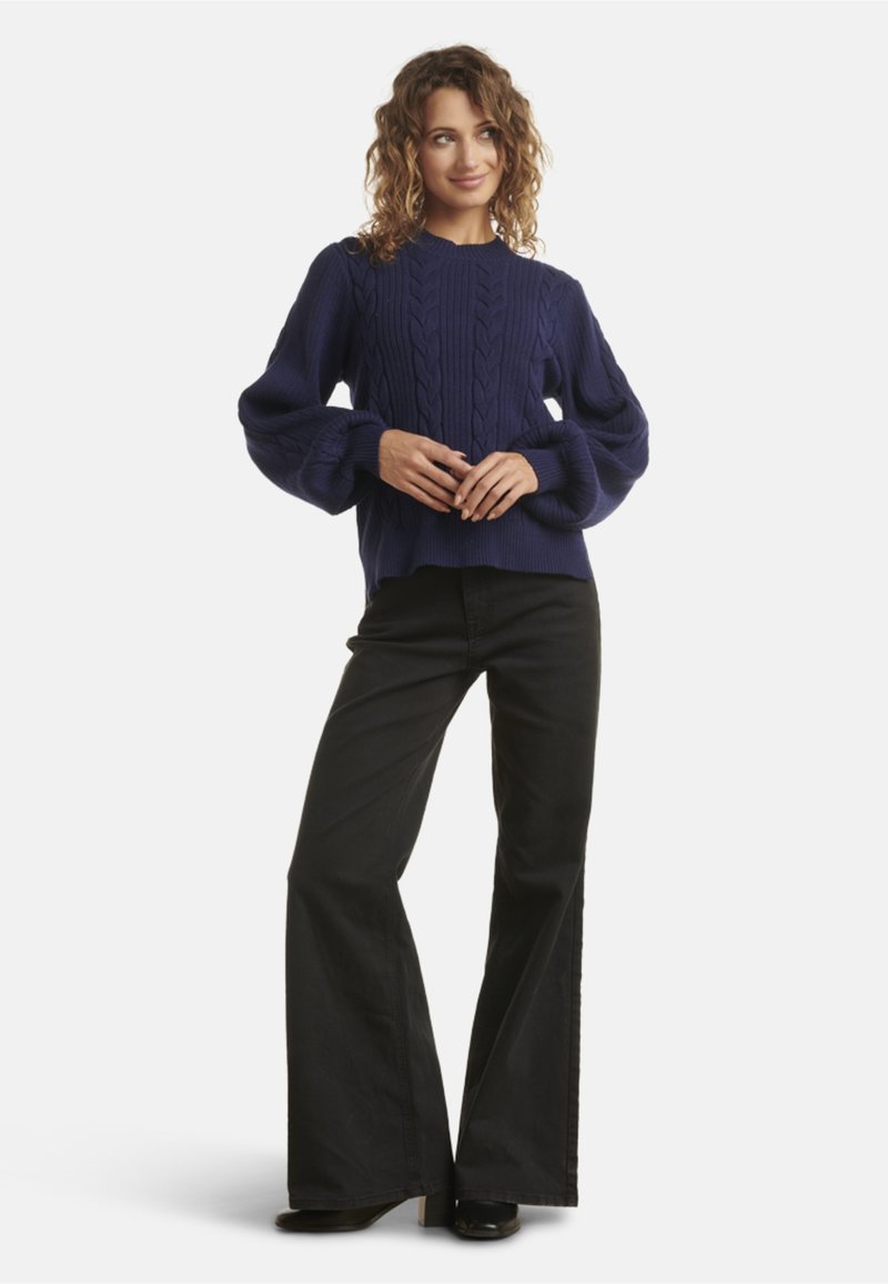 Maglione blu navy a intreccio con maniche a palloncino, abbinato a pantaloni neri svasati e stivali con tacco. Tessuto morbido, vestibilità comoda.