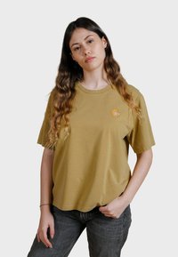 Camiseta de algodón color verde oliva con mangas cortas, cuello redondo y un pequeño logo bordado en naranja en el lado izquierdo del pecho.
