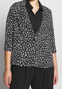 Blazer noir à imprimé léopard blanc, avec un col cranté et des manches trois-quarts, assorti à une chemise noire en dessous.