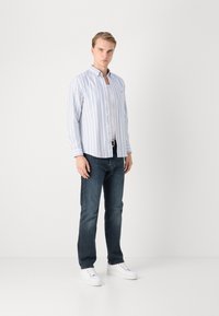 Gestreiftes Hemd in Blau und Weiß, kombiniert mit dunklen Jeans und weißen Sneakern. Das Hemd hat lange Ärmel und eine lockere Passform.