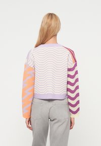 Πλεκτό  πουλόβερ με κοντό σχεδιασμό, ζιγκ ζαγκ μοτίβα σε λιλά, πορτοκαλί και μοβ, με ριμπ μανσέτες και στρογγυλή λαιμόκοψη.