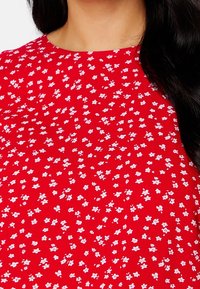 Tissu rouge avec un petit motif floral blanc, présentant un col rond et une surface texturée. Convient pour un usage décontracté.
