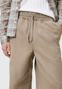 Beige, lätta byxor med elastisk midja och snörning. Tyget har en slät yta och har två sidofickor.