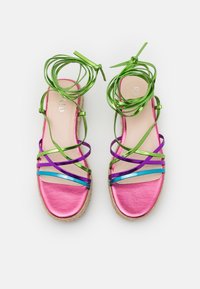 Sandales espadrilles métalliques roses avec des lanières irisées multicolores. Elles possèdent une semelle en jute tissé et des liens délicats en ruban.