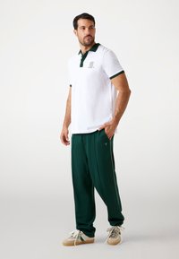 Weißes Poloshirt mit grünen Akzenten, kombiniert mit grünen Jogginghosen. Verfügt über ein Logo auf der Brust und hat einen lässigen Schnitt. Leichter, strukturiert Stoff.
