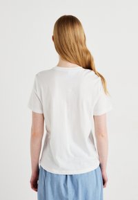White cotton t-shirt with short sleeves, round neckline, and a relaxed fit. Smooth texture, worn with light blue fabric bottom.