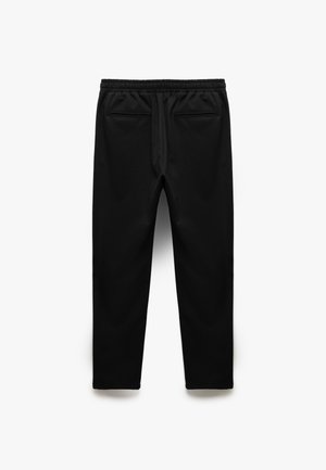 Pantaloni da jogging neri realizzati in tessuto morbido. Caratterizzati da una vita elastica, due tasche laterali e un design con gambe affusolate. Texture liscia.