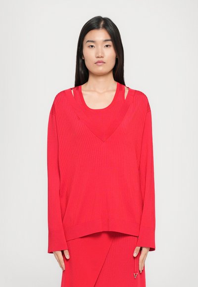 Red ribbed oversized sweater with cut-out shoulder detail, long sleeves, deep V-neckline, and a straight hem.