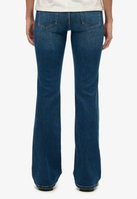 Jeans acampanados en un lavado medio, con una cintura estándar, dos bolsillos traseros y una textura de denim suave.