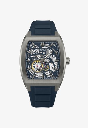 Montre Kenneth Cole avec un boîtier en acier inoxydable argenté, un bracelet en caoutchouc bleu marine, un cadran squeletté multicolore et des index horaires audacieux.