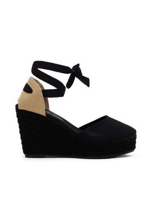 Alpargata cuña negra con tacón beige tejido, puntera cerrada y lazo negro que envuelve el tobillo.