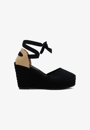 Alpargata cuña negra con tacón beige tejido, puntera cerrada y lazo negro que envuelve el tobillo.
