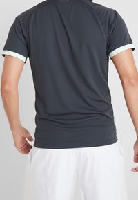 T-shirt de sport gris foncé à texture lisse, avec des accents vert clair sur les manches et un petit logo à l'arrière du col.