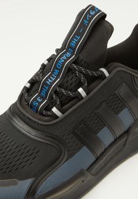 Schwarzer Sport-Sneaker mit strukturiertem Obermaterial, blauen Akzenten, dickem Sohlenprofil und einem markanten Schnürsystem samt Branding-Detail auf der Zunge.