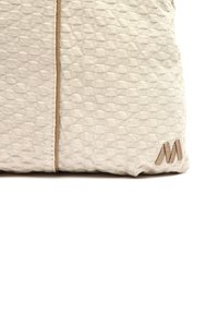 Cojín texturizado de color beige con un patrón tejido, que cuenta con una costura de acento marrón claro y un logotipo bordado marrón en el lado.