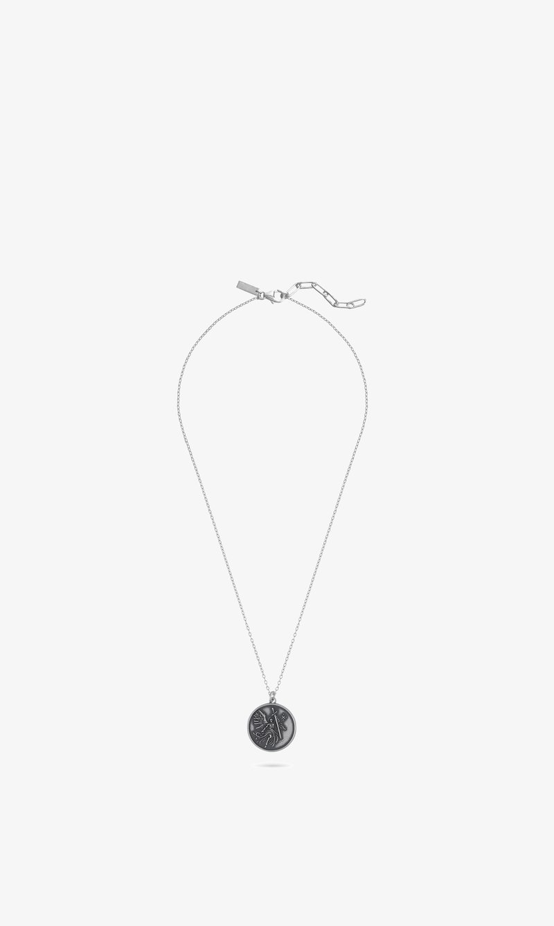 Collier en chaîne argentée avec pendentif rond présentant un design gravé d'une figure mythique ou ailée tenant une épée.