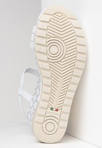 Sneaker bianco con un lato decorato, suola in gomma e design strutturato. Presenta un marchio e un indicatore di taglia, con una presa testurizzata.