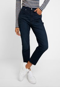 Mörkblå högmidjade jeans med en avslappnad passform, som har framfickor och en klassisk knäppning, tillsammans med vita sneakers.