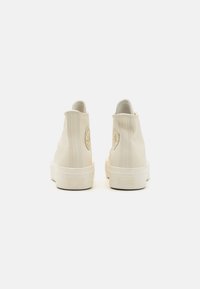 Sneakers alte in pelle color crema con una finitura strutturata, caratterizzati da un logo circolare e una suola in gomma bianca impressa con la scritta "ALL-STAR."