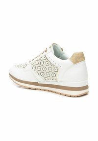 Zapatilla blanca con diseño floral perforado, acentos en beige y talón texturizado. Presenta suela de goma en color marrón y cordones redondos.