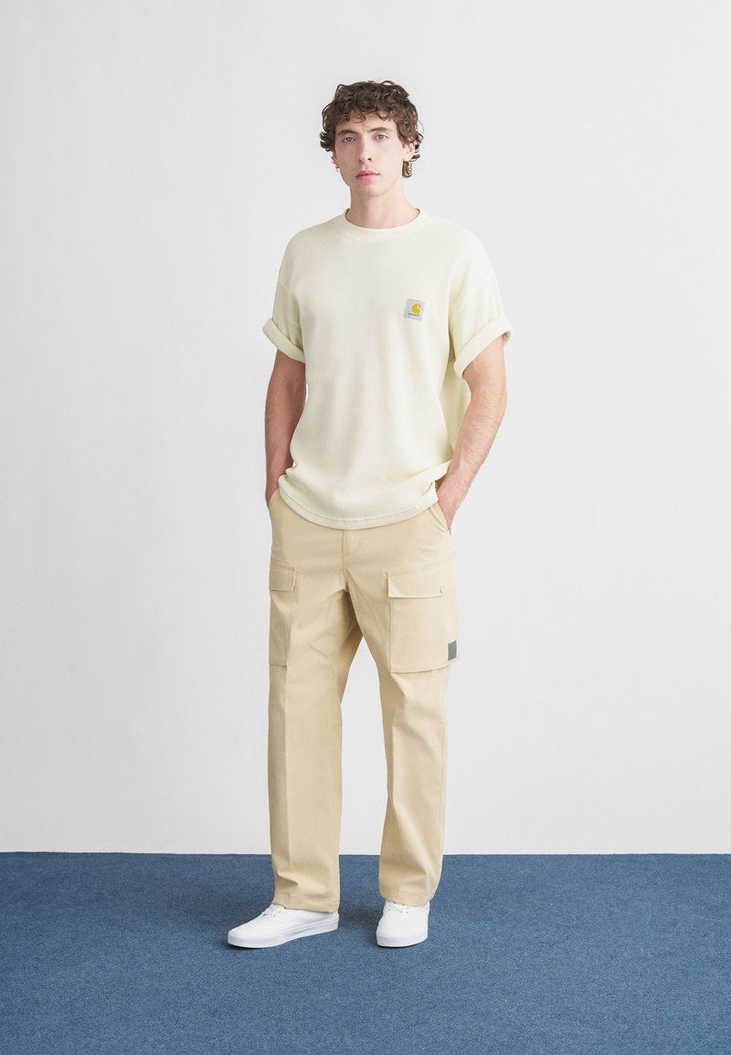 Light yellow textured short-sleeve shirt with rolled cuffs, beige cargo pants with side pockets, and white sneakers against a neutral background.