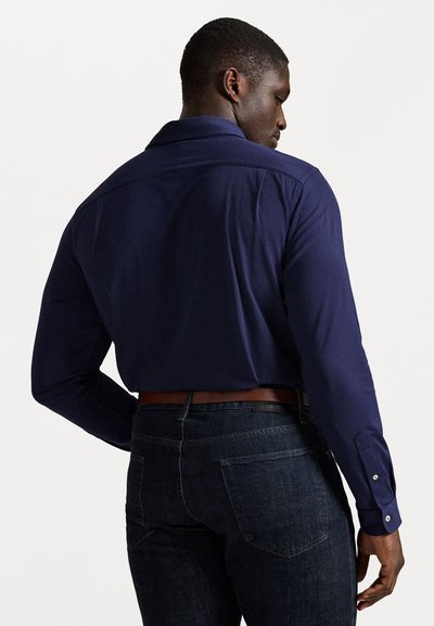 Ανδρικό μπορντό πουκάμισο με κουμπιά και μακριά μανίκια, σε κομψή γραμμή, συνδυασμένο με σκούρο τζιν. Διαθέτει απαλό ύφασμα και απλό σχέδιο.