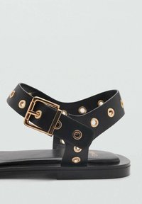 Sandalo nero con dettagli in oro, dotato di una fascia decorata con ritagli circolari e una chiusura a fibbia. Design della suola liscia e piatta.