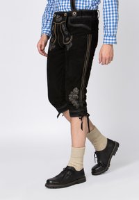 Black suede shorts with decorative silver embroidery, tied cuffs, and a matching black waistband; worn with a blue checkered shirt and black shoes.