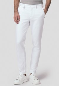 Białe bawełniane chinosy o wąskim kroju, z paskami na pasek i kieszeniami z przodu, zestawione z białymi trampkami. Gładka tekstura i czyste linie.