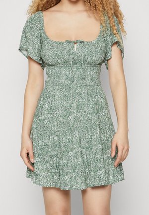 Groene bloemenjurk met korte fluttermouwen, gerimpelde bovenkant, vierkante halslijn en een sleutelgatdetail aan de voorkant. Aangesneden rok met een gestructureerd patroon.