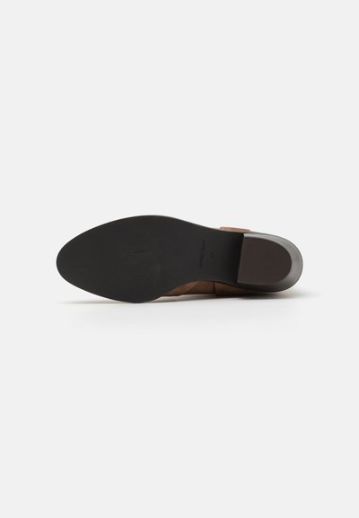 Boot de piele maro cu o talpă plată neagră și toc pătrat, prezentat din partea de jos pe un fundal alb.