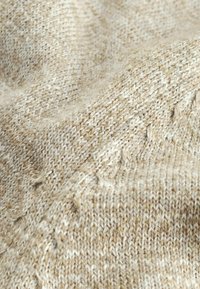 Beżowa dzianina o teksturowanym wzorze, z włóknami jaśniejszych i ciemniejszych nici, tworząca miękki, ciepły wygląd.