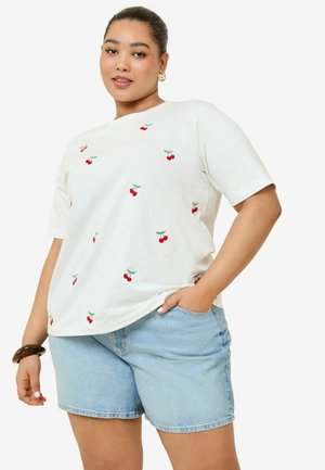 Camiseta blanca de manga corta con bordado de cerezas rojas dispersas, combinada con pantalones cortos de mezclilla azul claro y una pulsera decorativa.