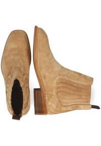 Botines de ante en color beige con puntera cuadrada, paneles elásticos en los laterales y un tacón apilado. La costura decorativa en los lados añade textura.
